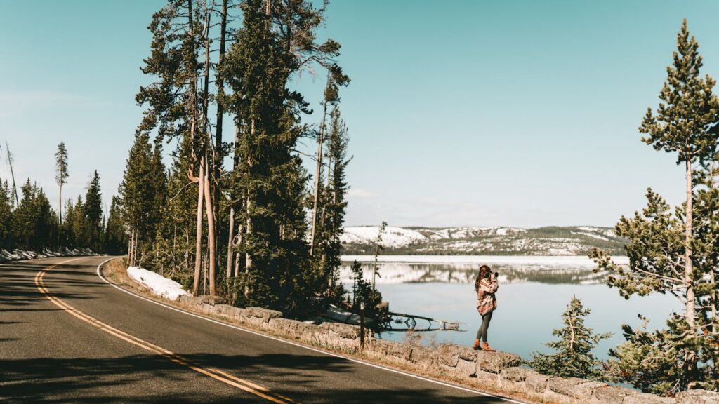 Woman takes photos by Yellowstone Lake with mountains and snow in winter.