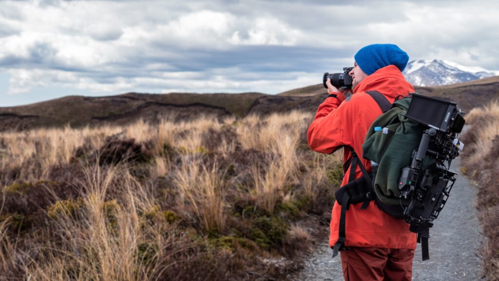 Person wearing backpack and holding DSLR camera.