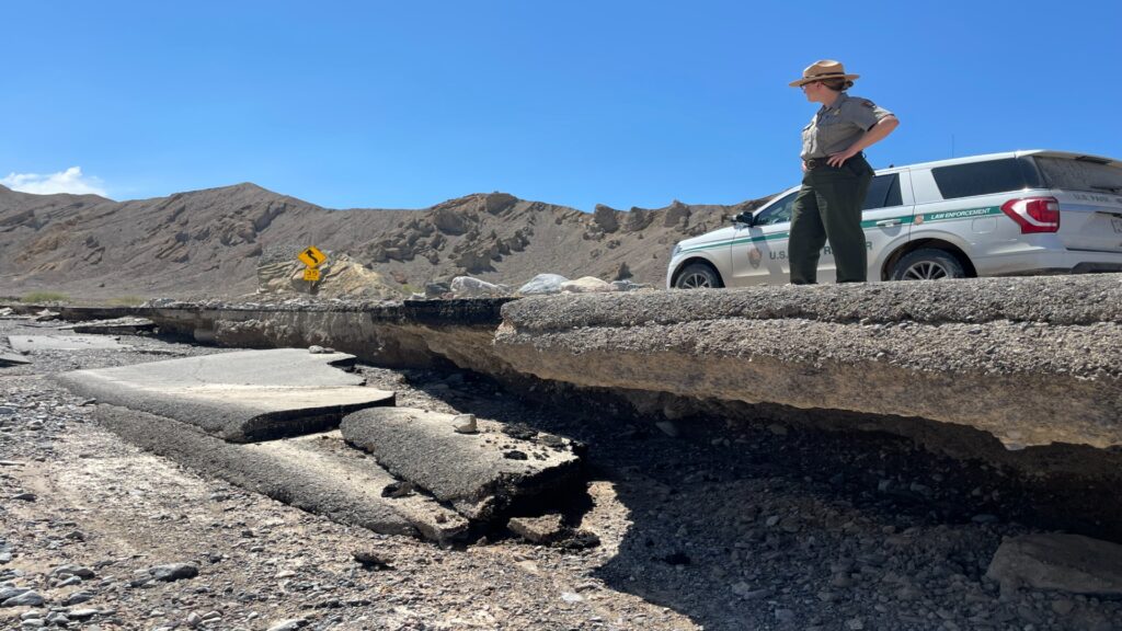 A park ranger stands beside a truck on a dusty road in Death Valley, surrounded by arid desert landscape.