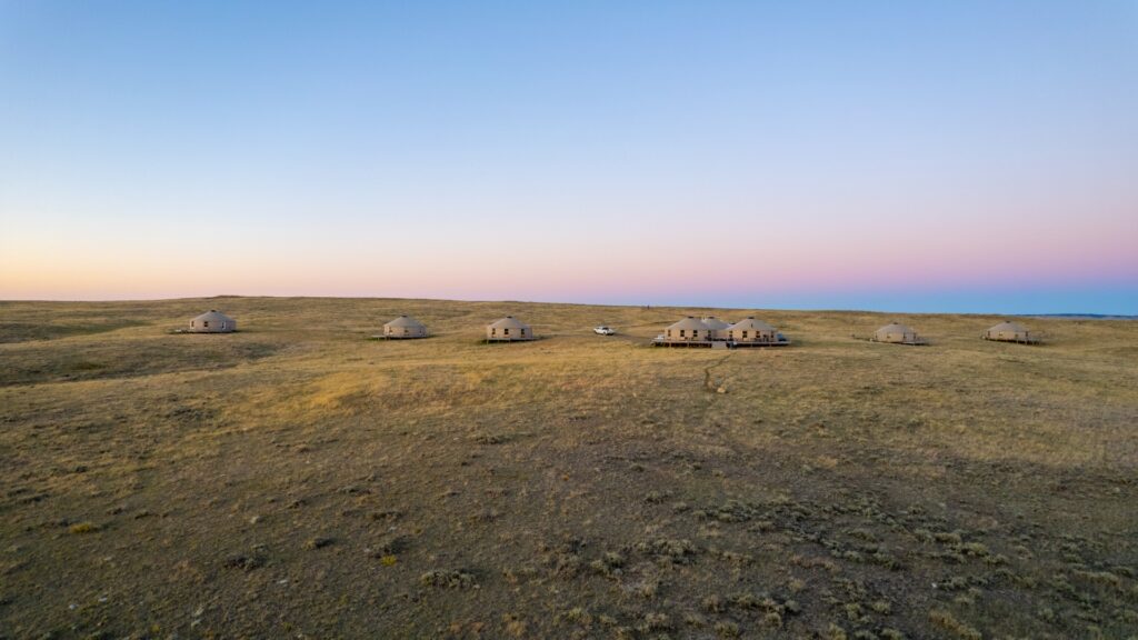 Yurts dotting a hillside in a wide-open field, showcasing the serene beauty of the American Prairie Reserve.