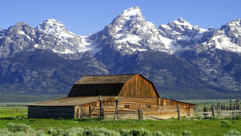 A rustic barn stands in the foreground, framed by the majestic peaks of Grand Teton National Park in the background.
