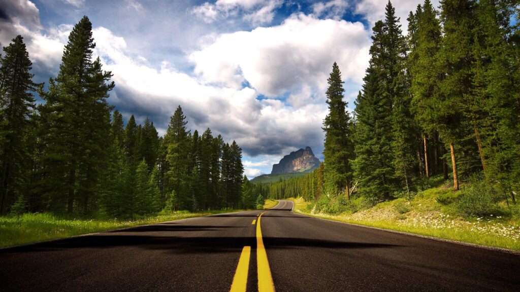 Scenic view of Bow Valley Parkway, highlighting an empty road lined with trees, leading to stunning mountains in the background.