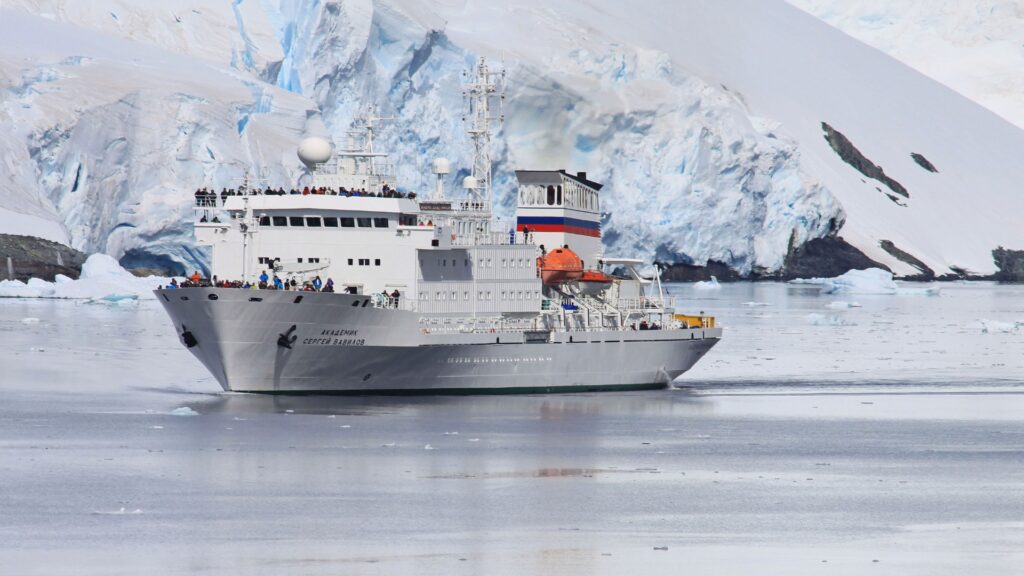 A sizable vessel floats in the frigid sea, representing the exploration efforts of the International Association of Antarctica Tour Operators.