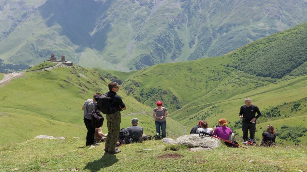 A group of people stands on a hill, gazing at a scenic valley below, enjoying the panoramic view together.