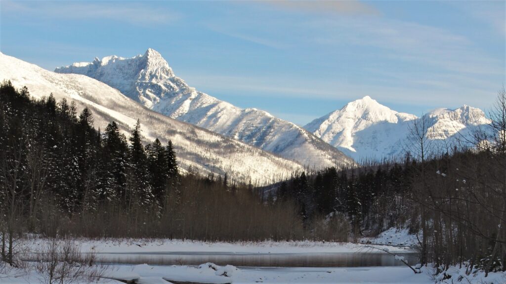 A picturesque river meanders through a snowy forest, set against the stunning mountain backdrop of Glacier National Park.