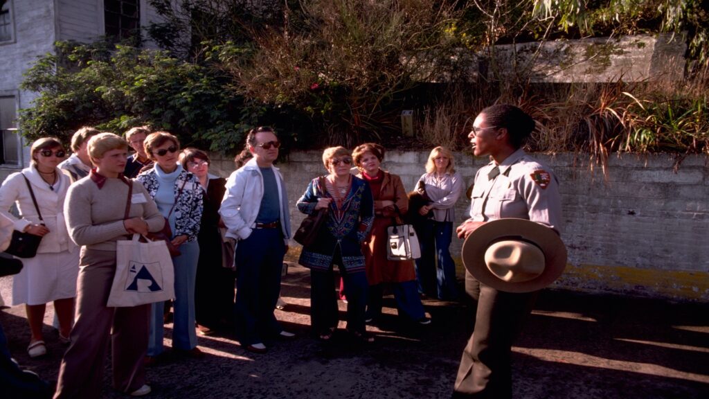 A group of people gathers around a man wearing a hat, engaged in conversation and sharing smiles.