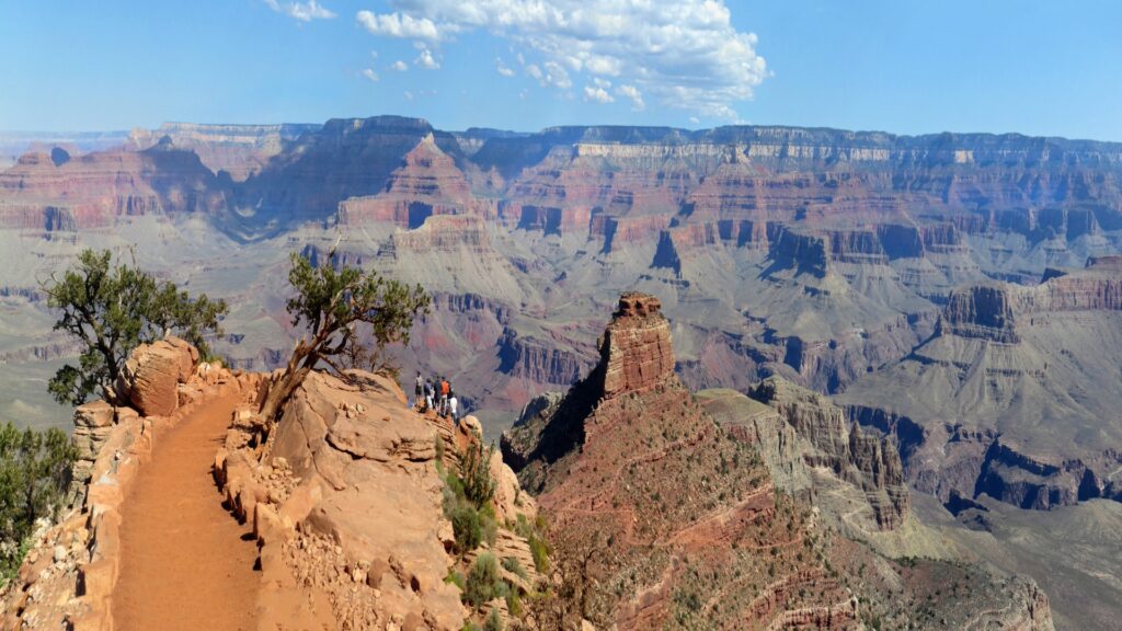 A park ranger engages with tourists at the Grand Canyon, surrounded by dramatic cliffs and vibrant colors of the canyon landscape.