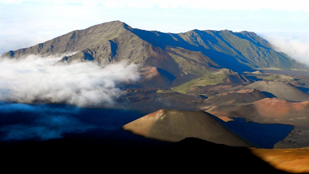 A panoramic view of a majestic mountain range partially shrouded in fluffy white clouds against a clear blue sky.