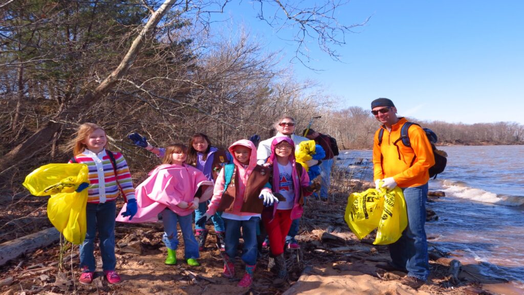A cheerful group all holding yellow bags, capturing a moment of fun and camaraderie by the sea.