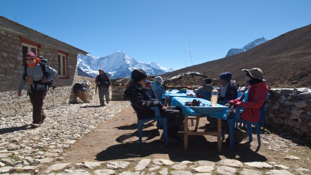 Groups of people relax at tables outside, sharing conversations and enjoying the pleasant weather in a lively setting.