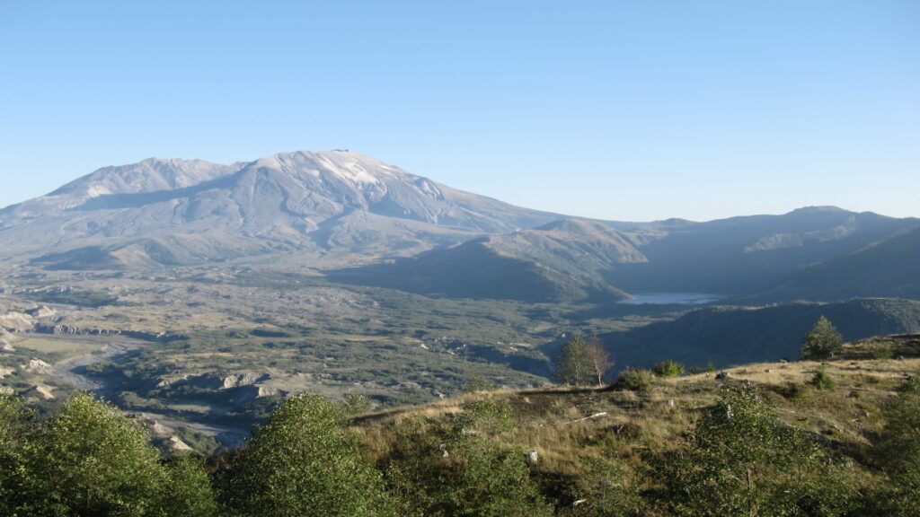 Mount St. Helens rises majestically, featuring its iconic crater and lush green slopes against a backdrop of distant mountains.