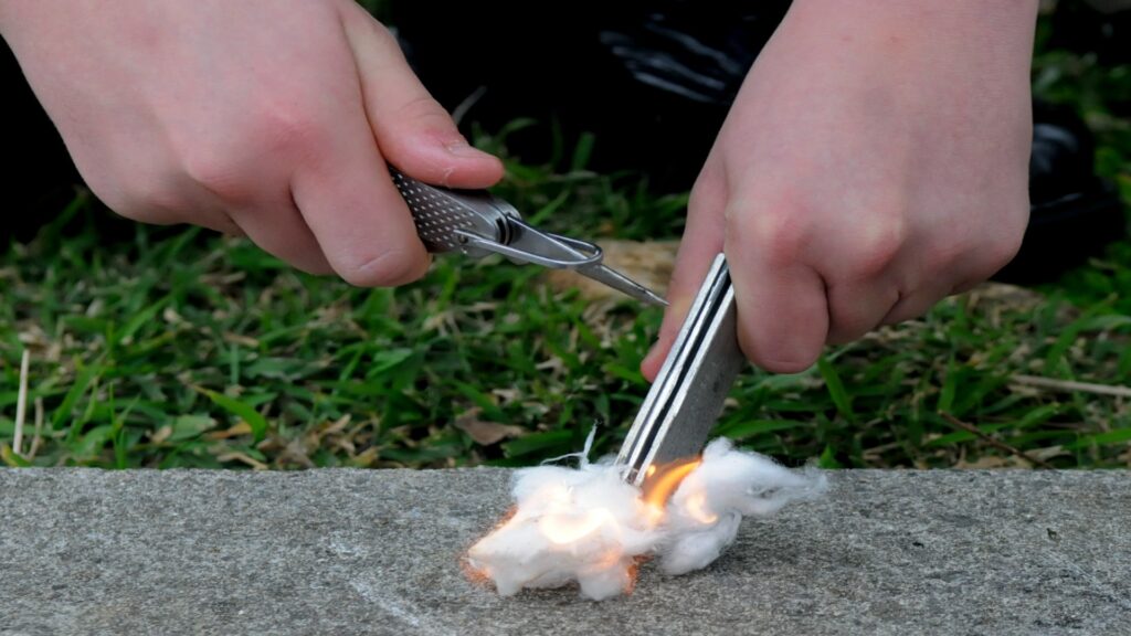 A close-up of hands cutting cotton with scissors, illustrating the preparation for fire-starting techniques.