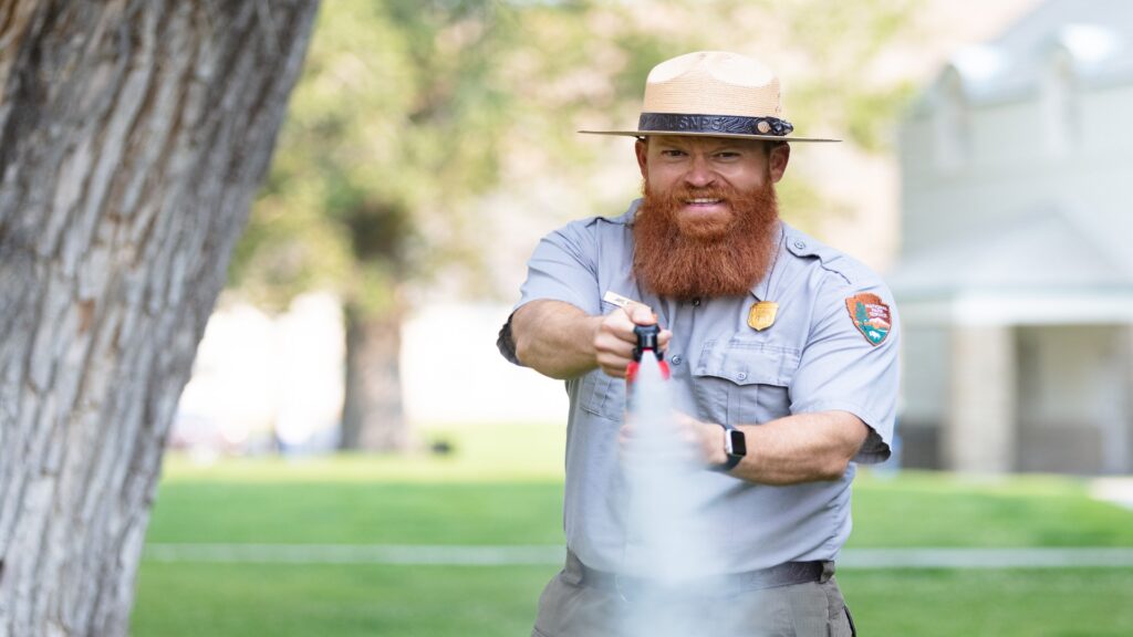 A man with a beard uses a bear spray, showcasing ranger skills in environmental care and conservation.