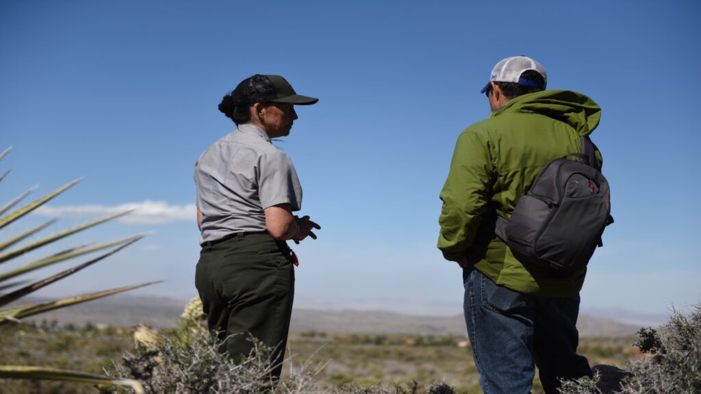 Two park rangers in the desert, gazing intently at a distant landmark under a clear blue sky.