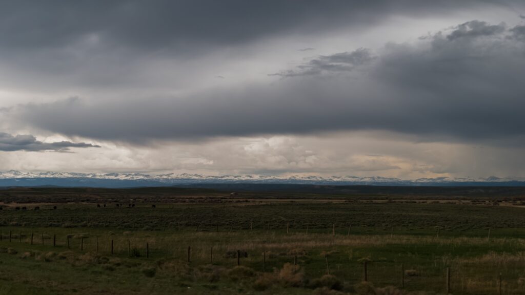 A dramatic stormy sky filled with dark clouds hovers over the mountains, creating a striking contrast with the plains.