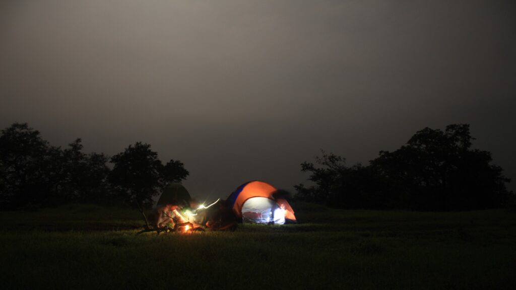 A tent radiates light in the dark, surrounded by a starless night sky, offering a sense of warmth and shelter.