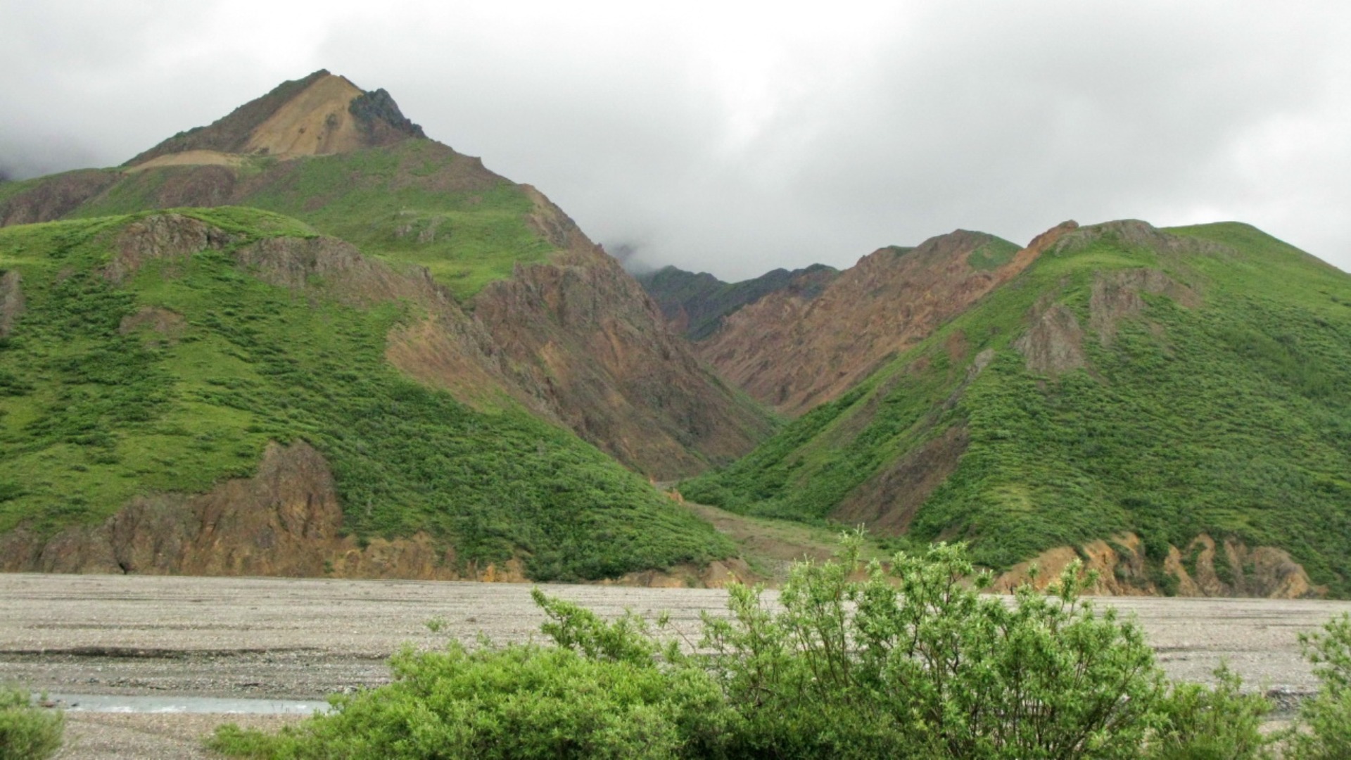A breathtaking view of a mountain range featuring rich vegetation and a tranquil river flowing gracefully through the terrain.