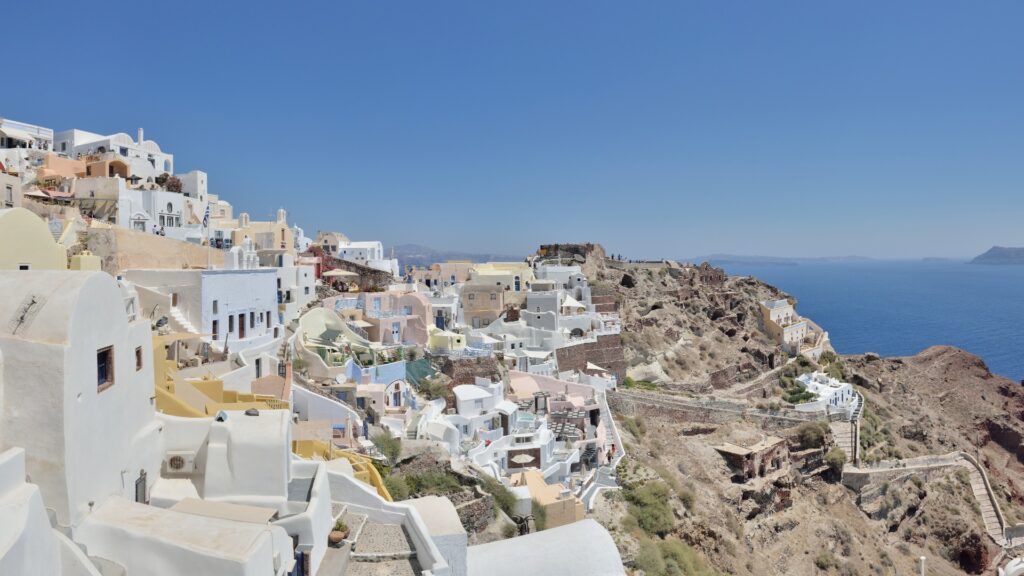 Panoramic view from a hilltop in Santorini, showcasing the vibrant blue sea and whitewashed buildings against a clear sky.
