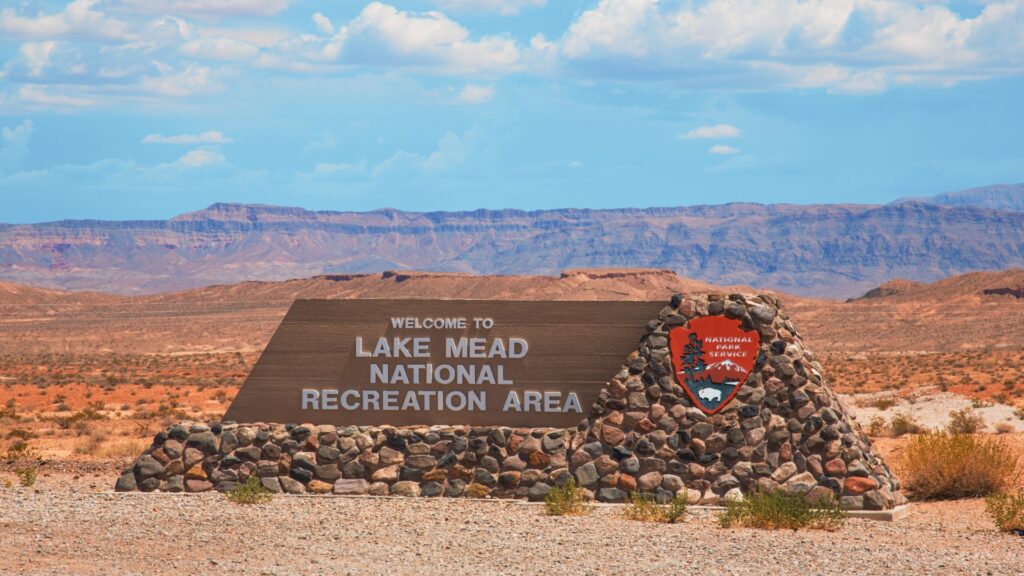 A sign displaying "Lake Mead National Recreation Area" against a natural backdrop, welcoming visitors to the scenic location.