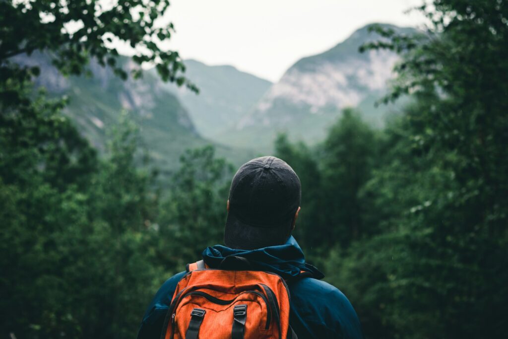 A hiker with a backpack stands in awe, admiring the towering mountains that rise dramatically in the background.