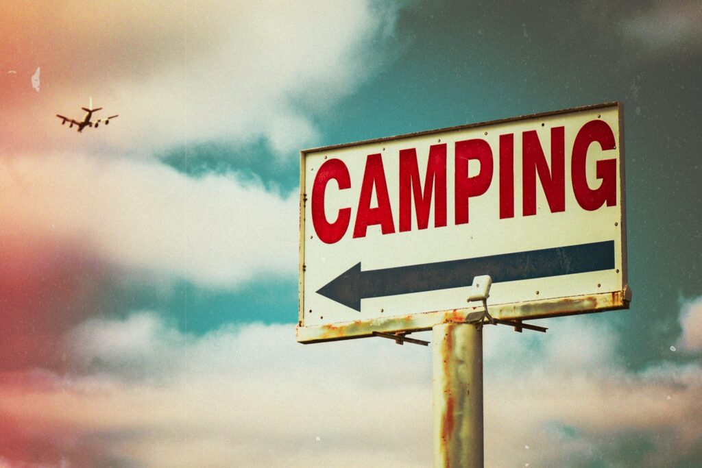 A wooden sign with the word "Camping" painted in bold letters, surrounded by trees and a serene outdoor setting.