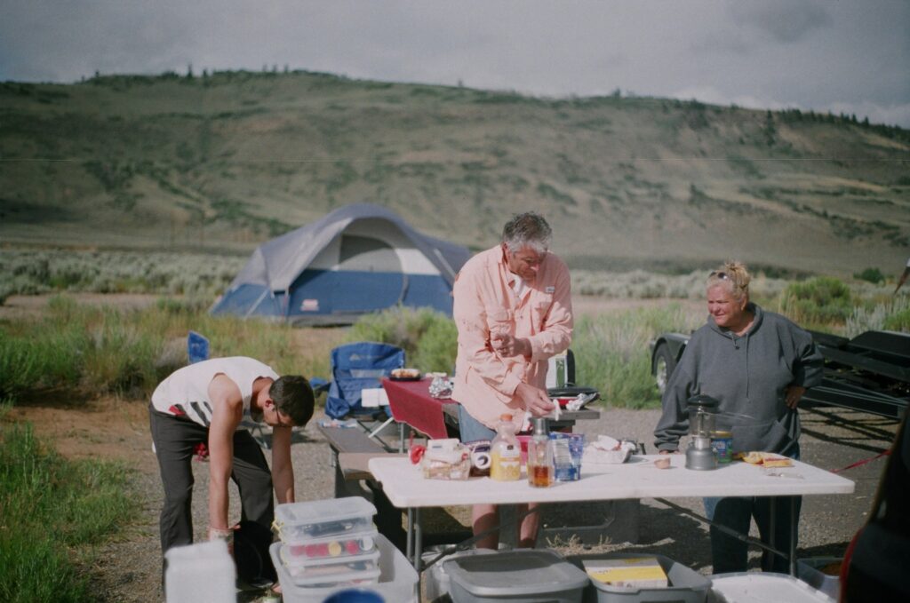 A lively group of people in a camp kitchen setup, collaborating around a table while cooking and enjoying the camping experience.