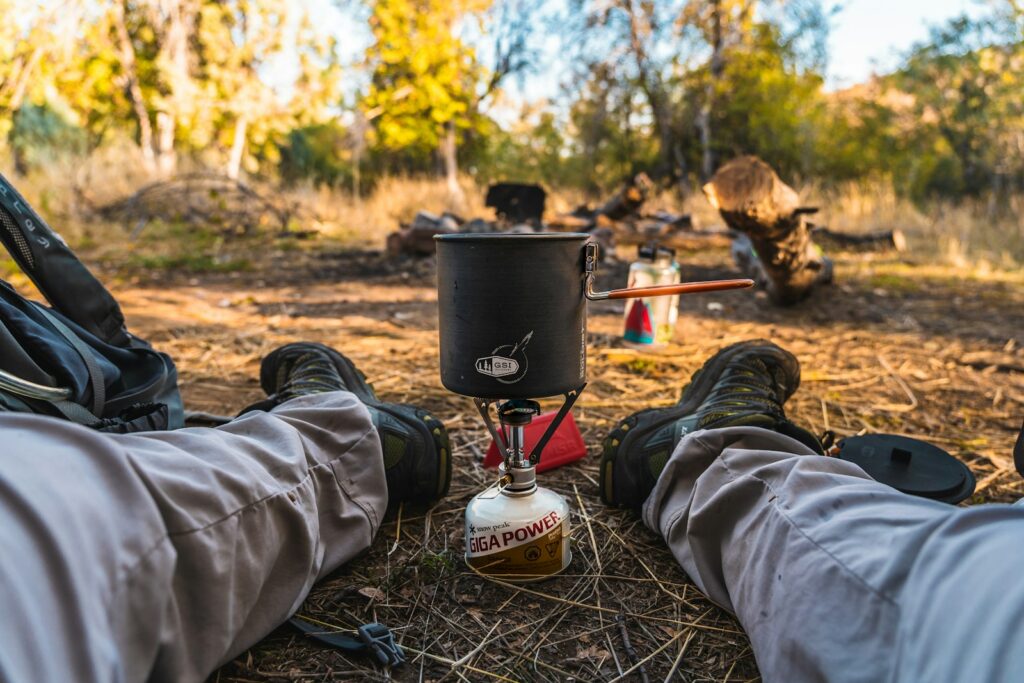 Person in gray pants sitting on ground with black kettle on top.