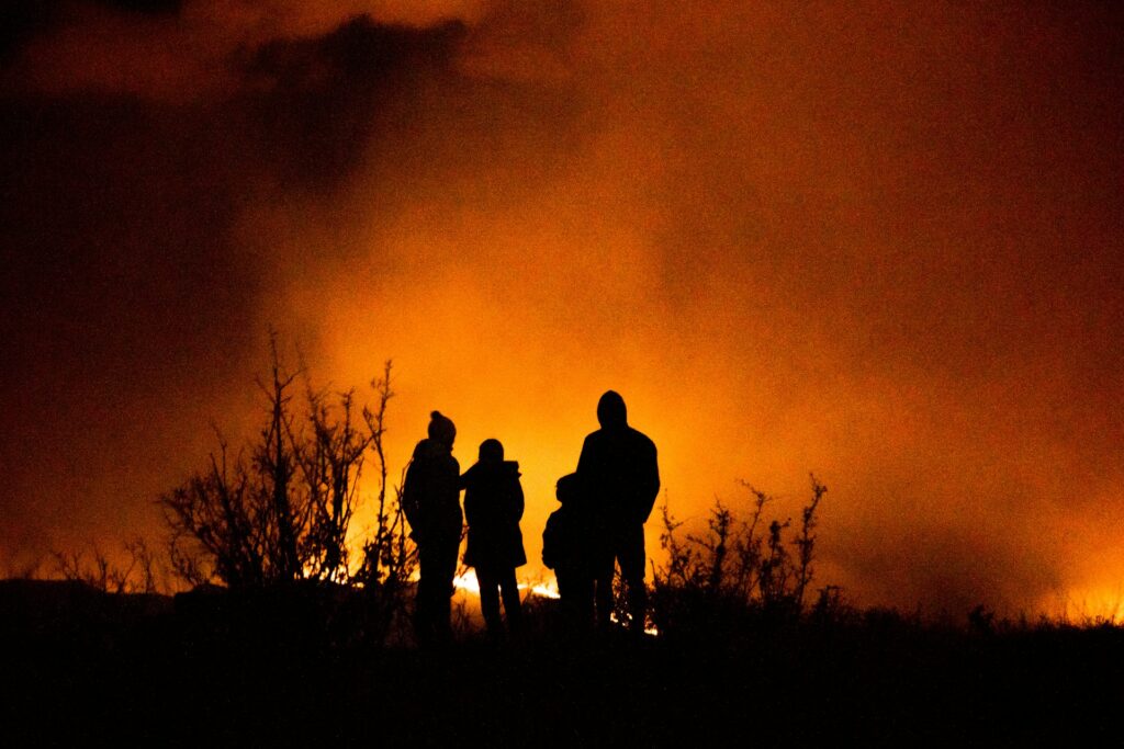 People congregate around a flickering fire, their faces glowing in the night, sharing stories and warmth.