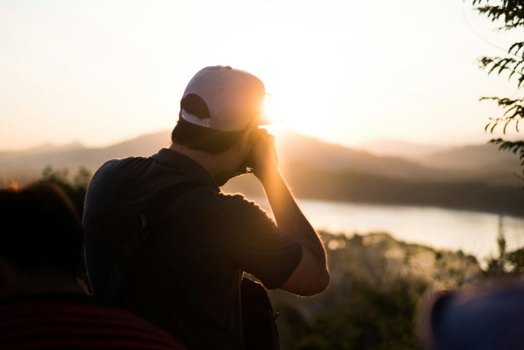 A man photographs a stunning sunset reflecting on a serene lake, surrounded by nature's colorful display.