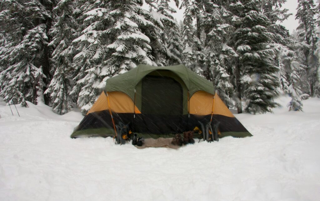 A vibrant tent is pitched in a snowy field, contrasting with the soft, white snowflakes covering the ground.