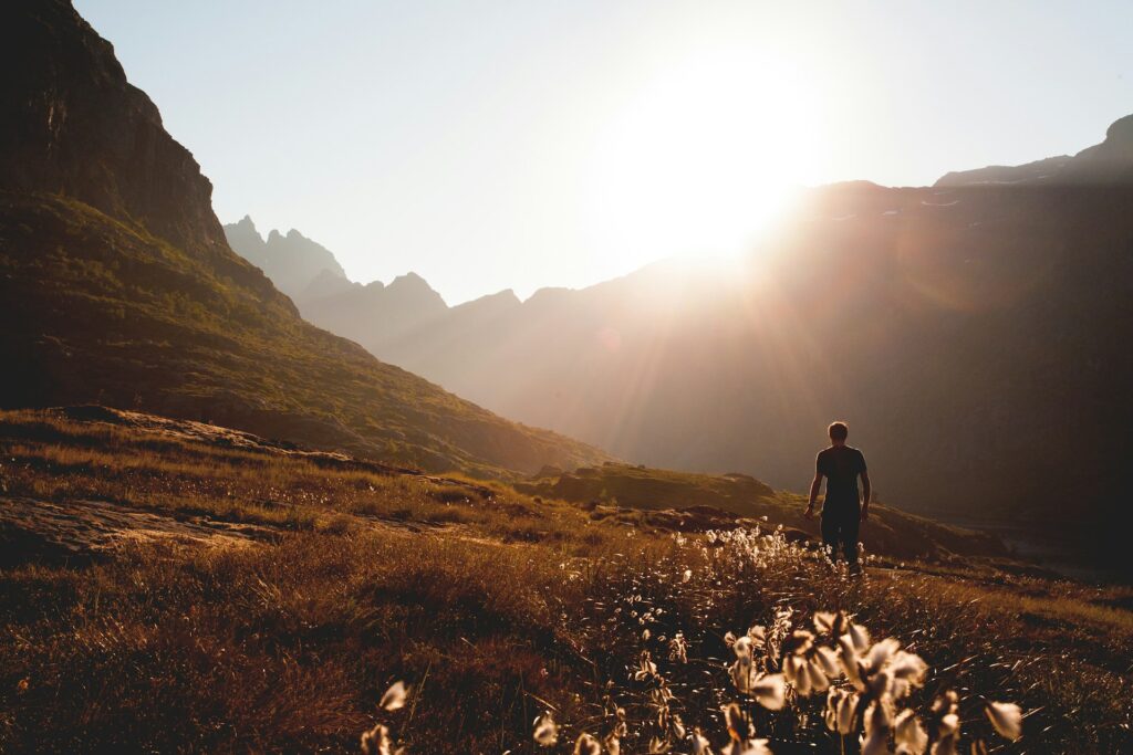 A lone hiker traverses a mountain path at sunset, surrounded by stunning hues of orange and purple in the sky.