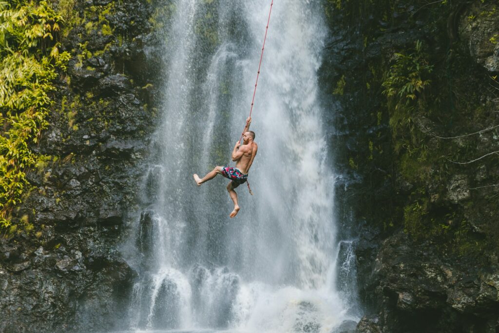 A man hangs from a rope against a backdrop of a stunning waterfall, capturing a moment of thrill and nature's beauty.