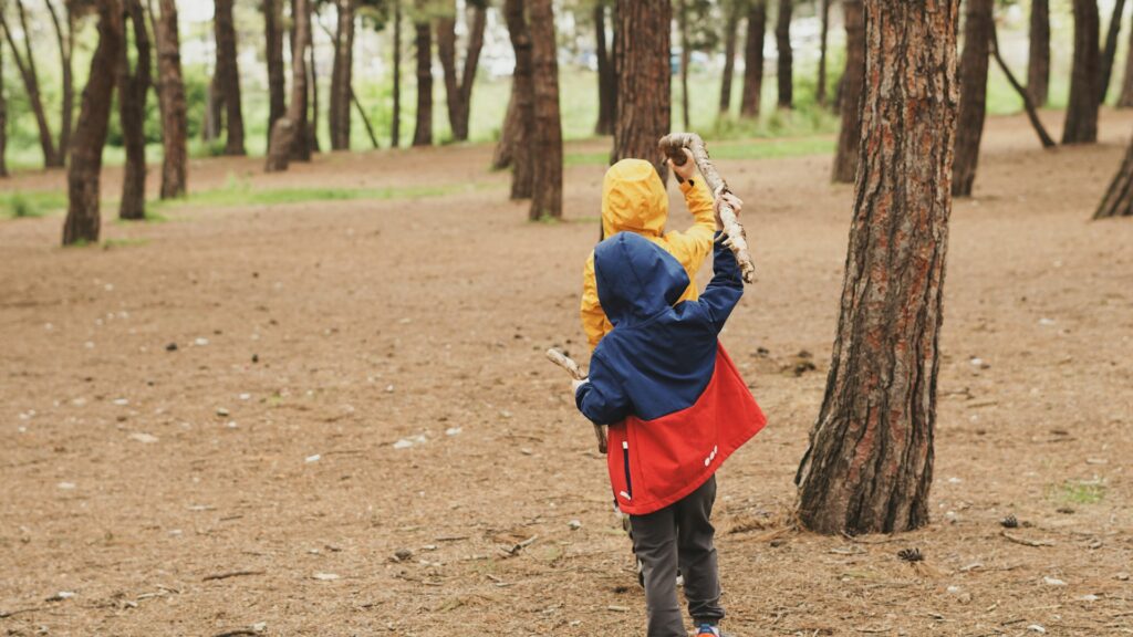 A boy and girl hiking together in a lush green forest, surrounded by tall trees and dappled sunlight.