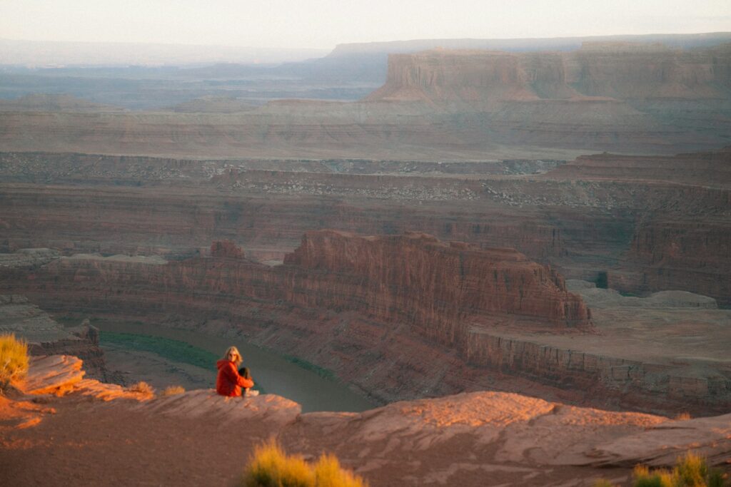 Person sitting, overlooking a stunning canyon landscape.