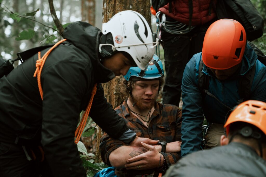 Mountain rescuers in helmets and jackets assisting each other while administering first aid to an injured climber.
