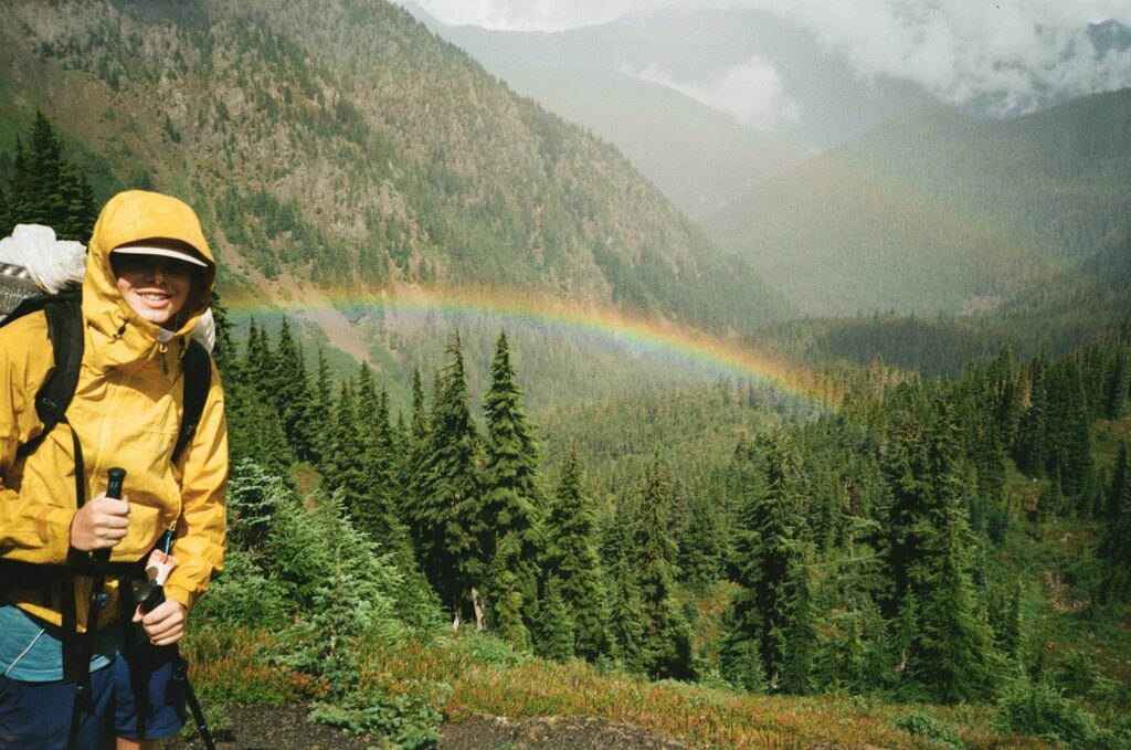 A man with a backpack and a backpack standing in front of a rainbow