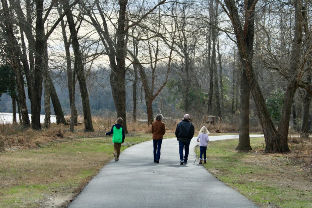 A family enjoys a leisurely walk on a wooded trail, enveloped by nature's beauty and the sounds of the forest.