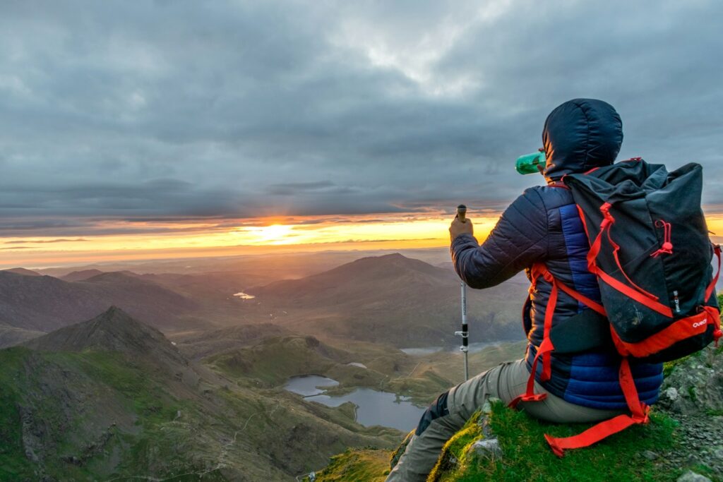 Man sitting on cliffhanger looking at mountain under gloomy clouds