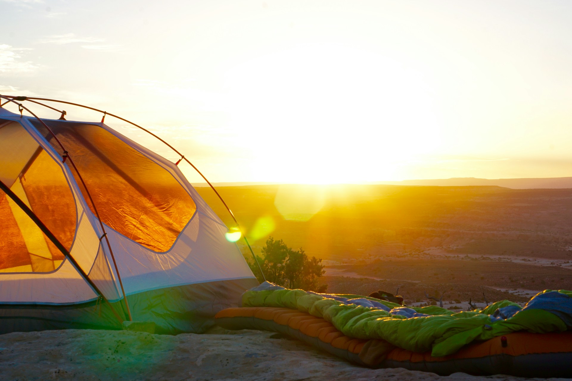 A tent and a sleeping bag are positioned on a hill, inviting outdoor adventure with a stunning view of the surrounding scenery.