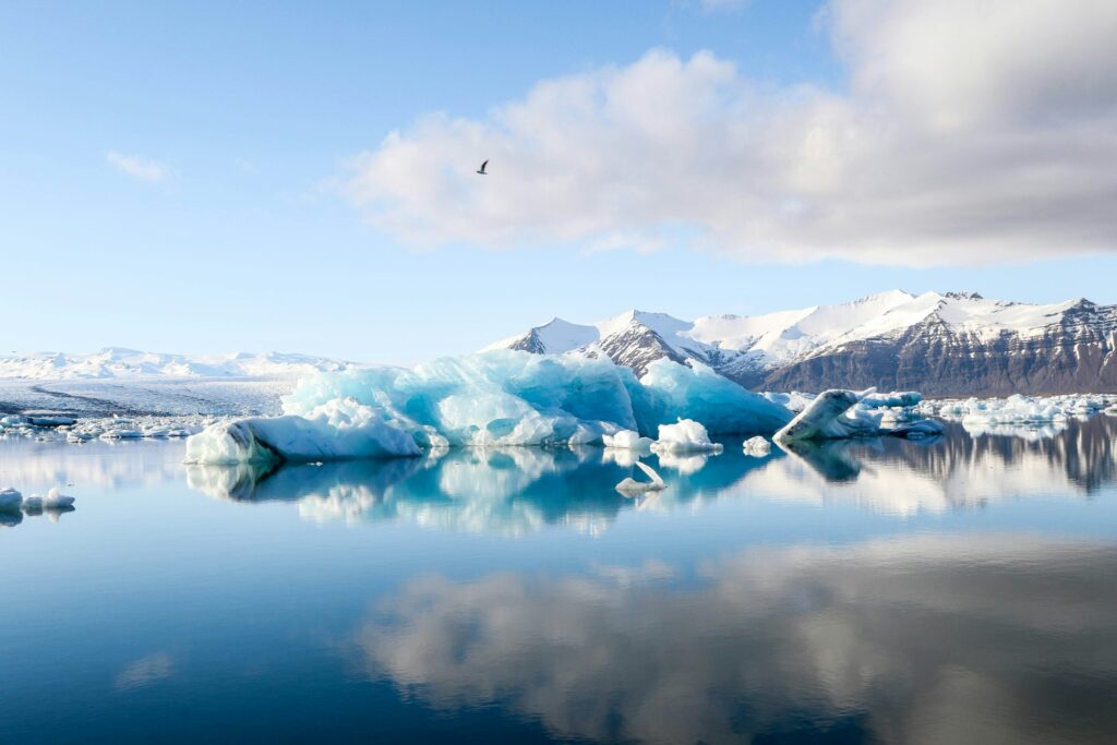 Icebergs glide through tranquil waters, set against a backdrop of rugged, snow-capped mountains.