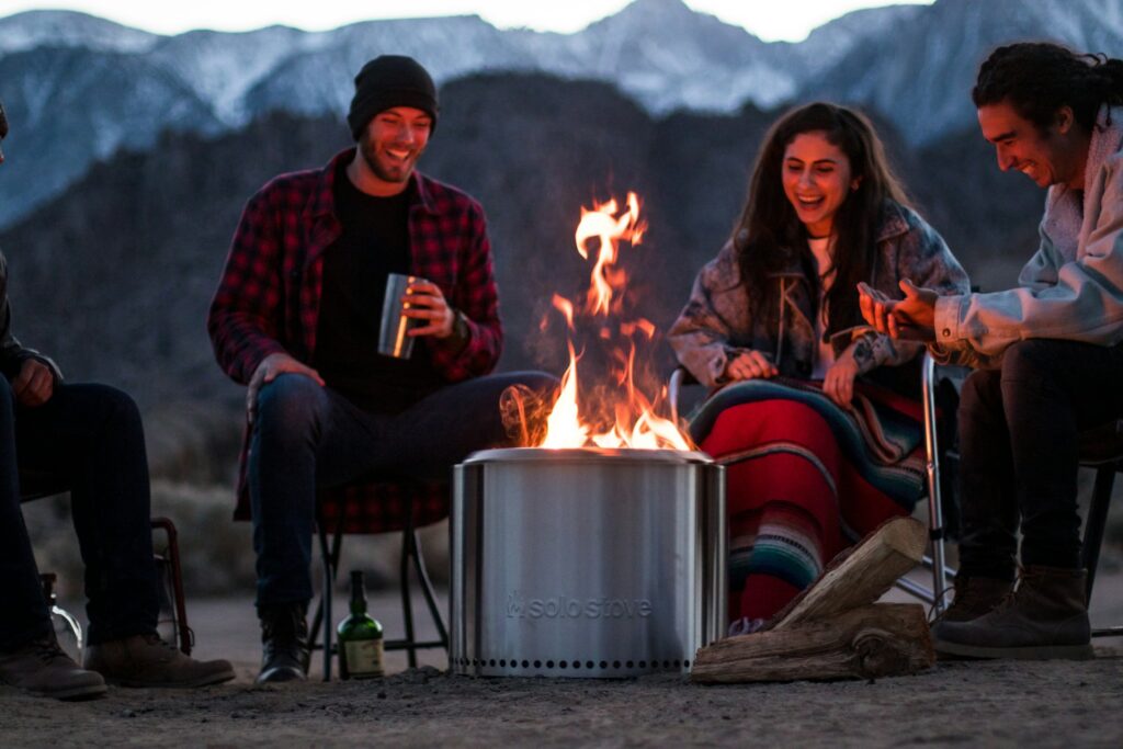 Four friends gather around a cozy fire pit, enjoying beers and laughter under a starlit sky.