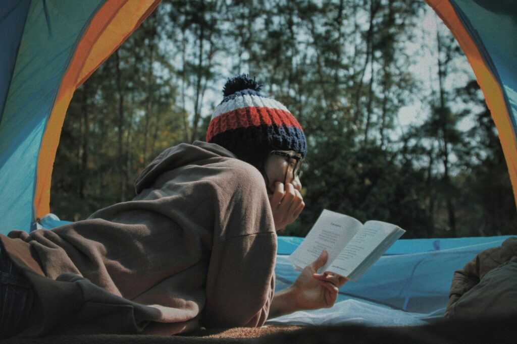 A person relaxes in a tent, deeply focused on a book, with the fabric walls softly framing their reading nook.