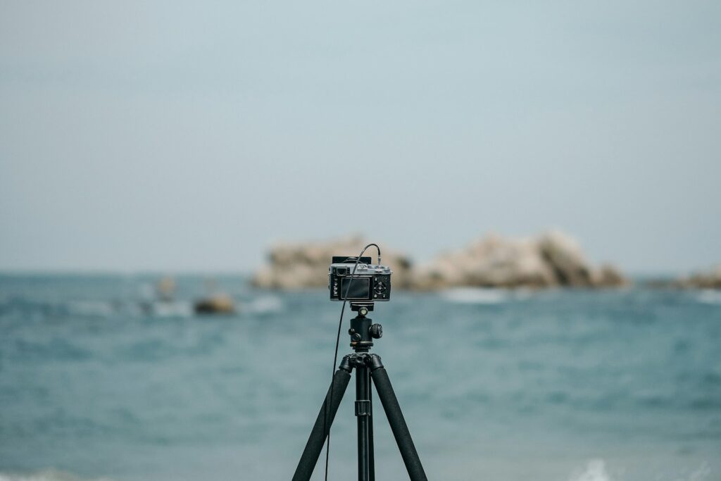 Black and silver camera on tripod on beach shore during daytime.
