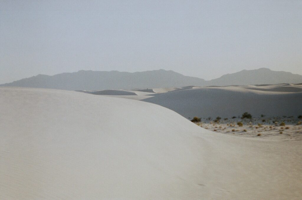White sand with green grass and mountains in the distance