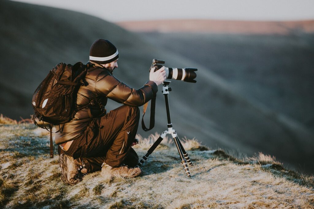 man taking photo using black and white DSLR camera on hill at daytime