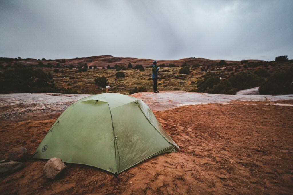A peaceful campsite with tents set against a backdrop of vibrant red cliffs and clear blue skies.