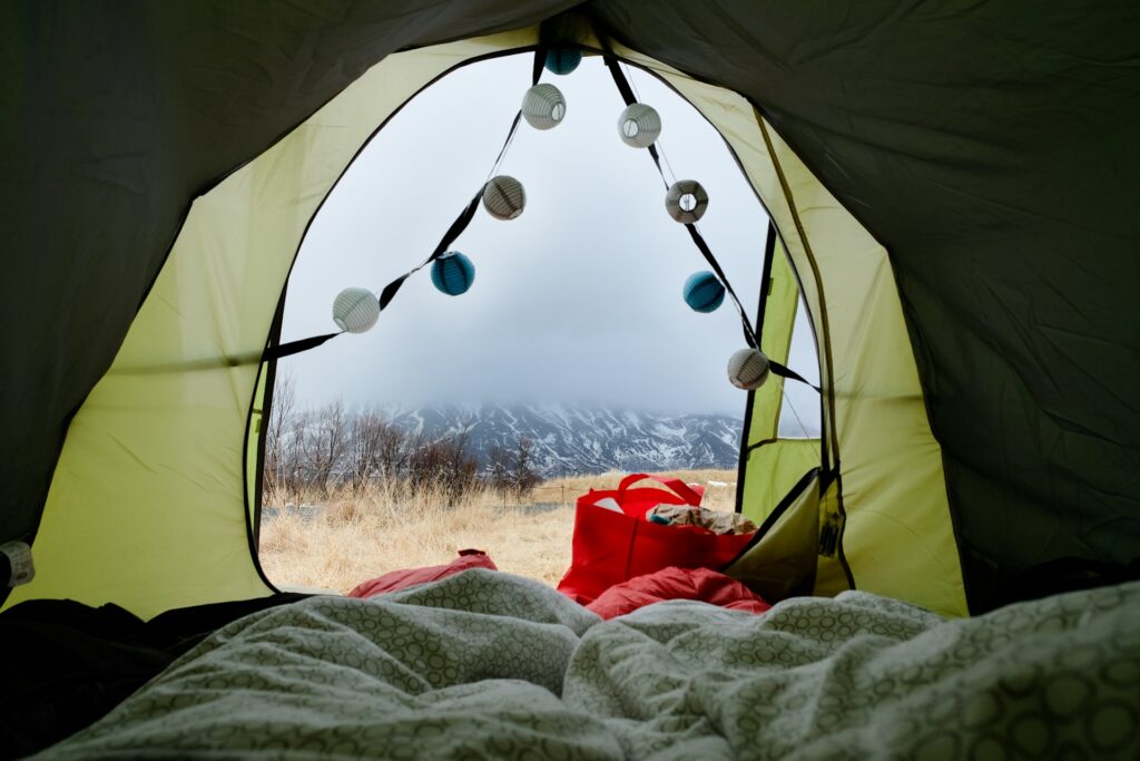 A person relaxes inside a tent, wrapped in a blanket with a bag beside them, enjoying a cozy camping experience.
