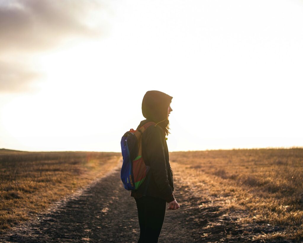 person wearing backpack standing on pathway during golden hour