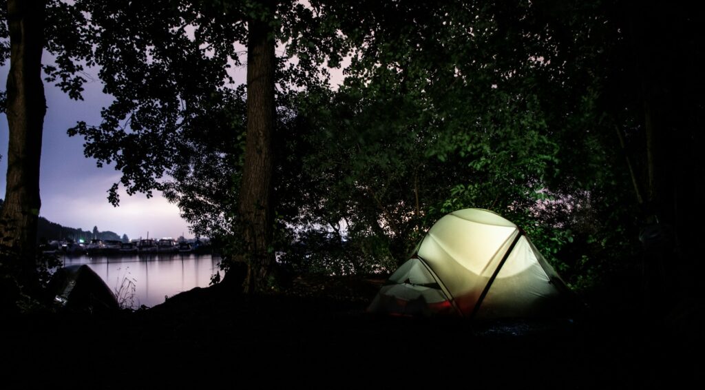 In the dark, a tent shines brightly near the water, enhancing the peaceful ambiance of the nighttime scene.