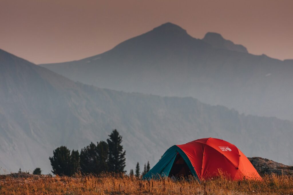 Red tent on brown grass field near green trees and mountain during daytime.